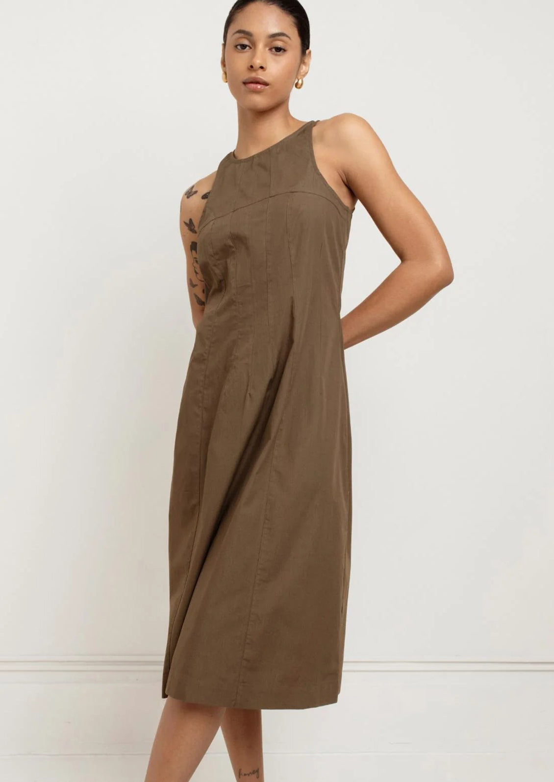 A person wearing a sleeveless dress in olive color.