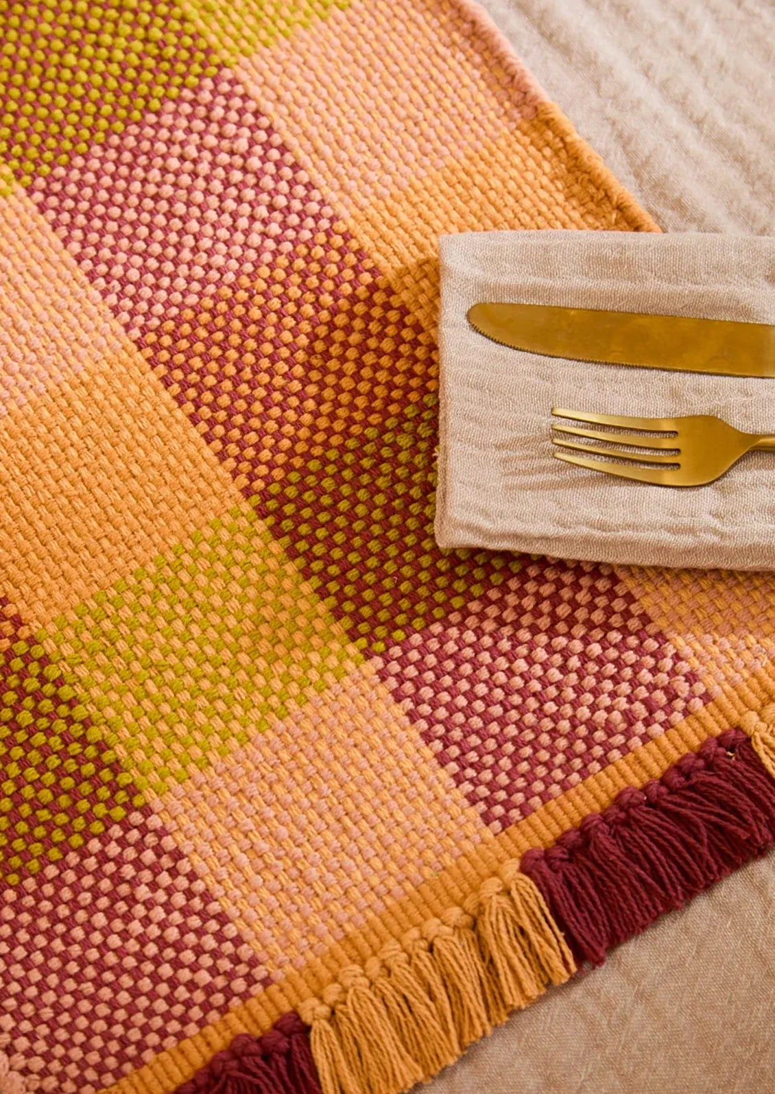 Colorful woven placemat with a gold fork and knife on a matching napkin.