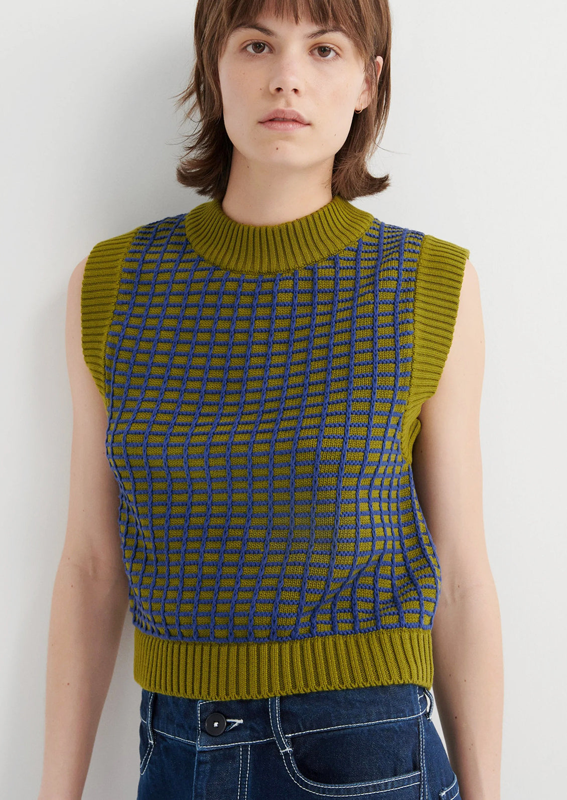 Person wearing a green and blue patterned sleeveless sweater against a white background