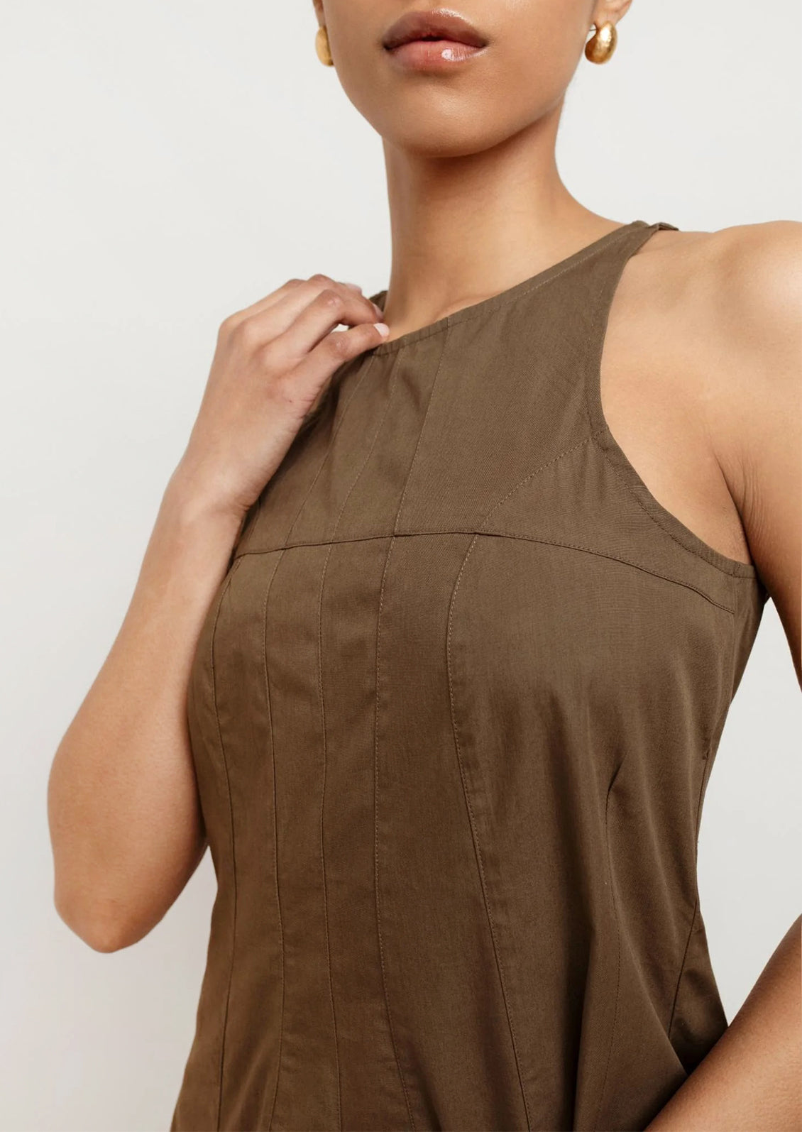 A person wearing a sleeveless dress in olive color.