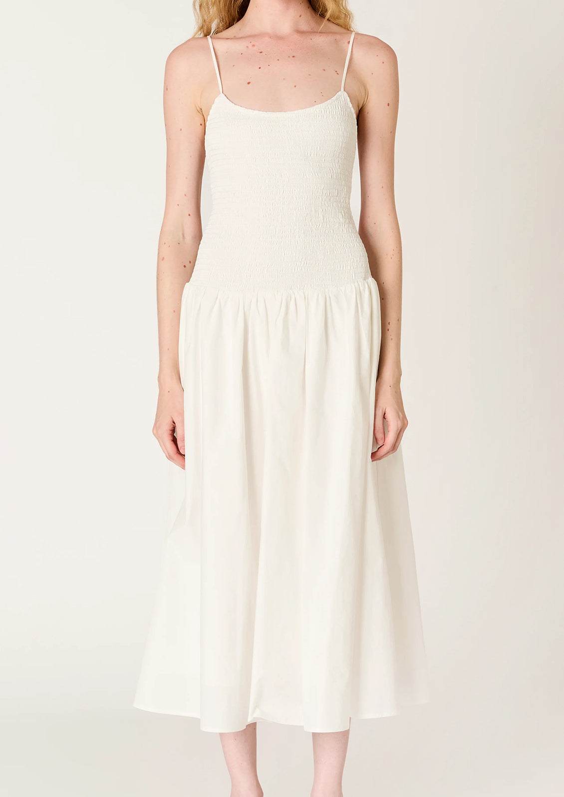 A person wearing a white dress with smocked bodice, full skirt and strappy open back.