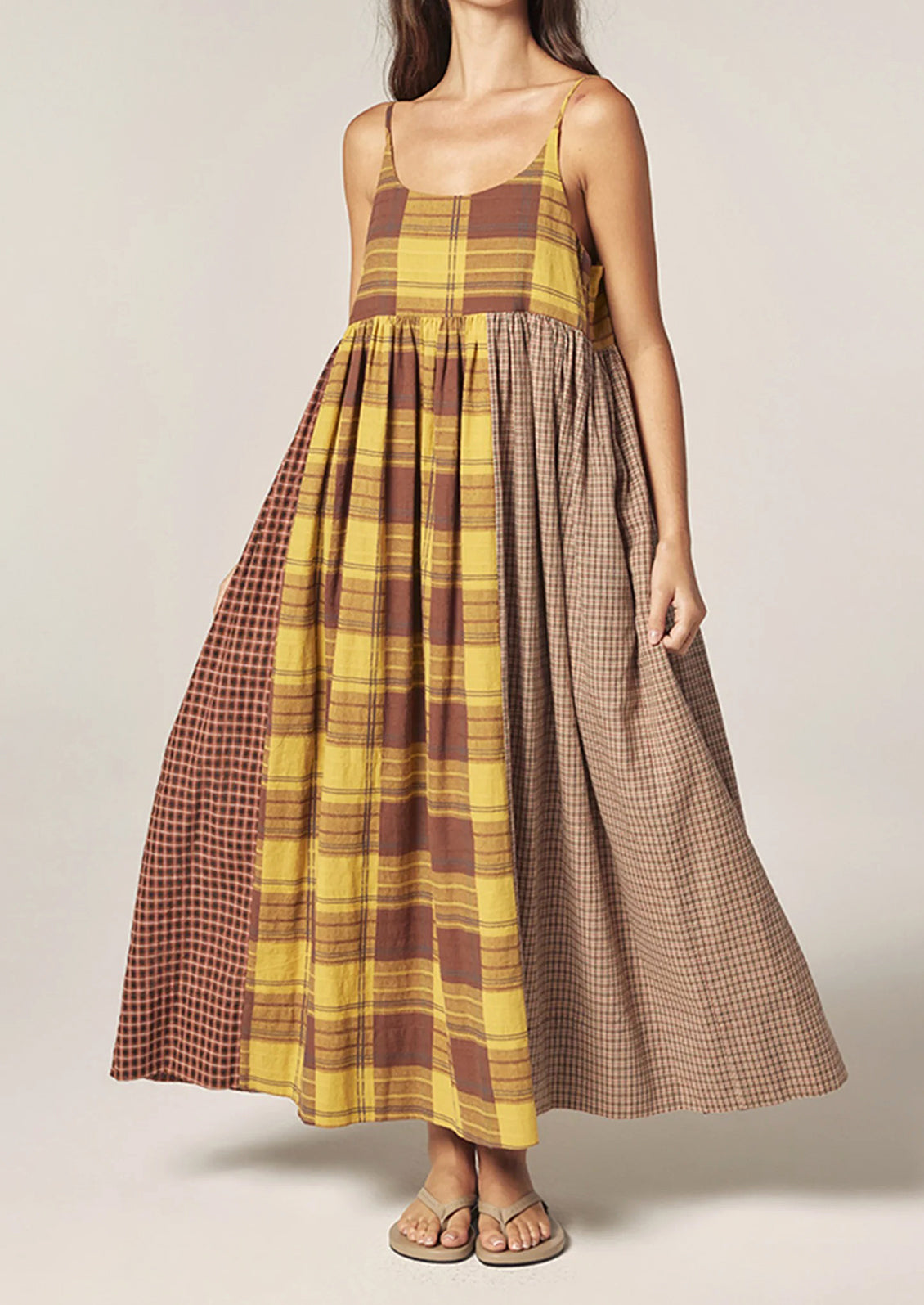 A person wearing a long plaid cotton dress in brown and yellow tones.