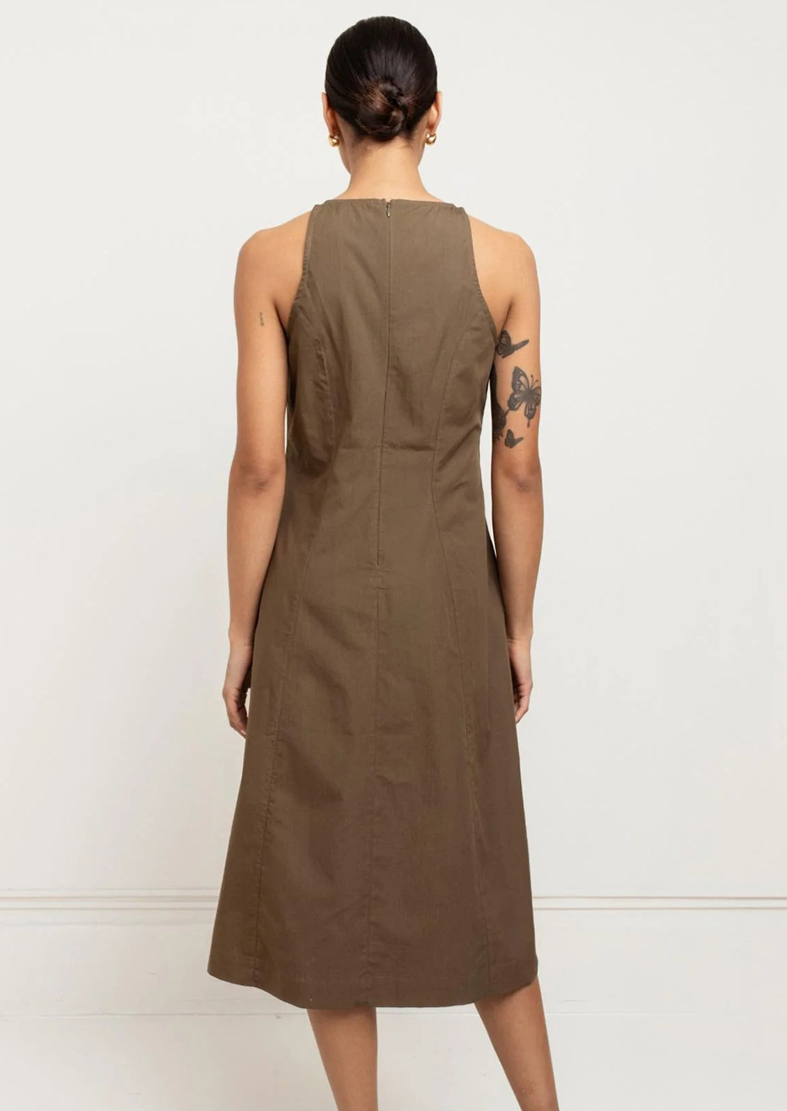 A person wearing a sleeveless dress in olive color.