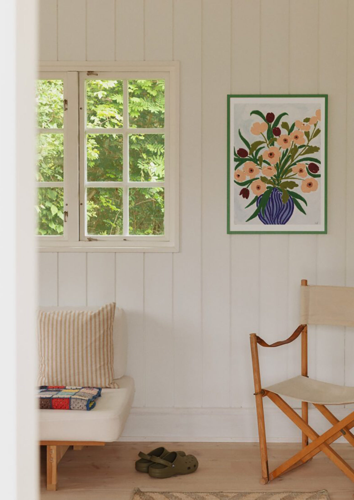 Room interior with a window, chair, and floral artwork on a white paneled wall.