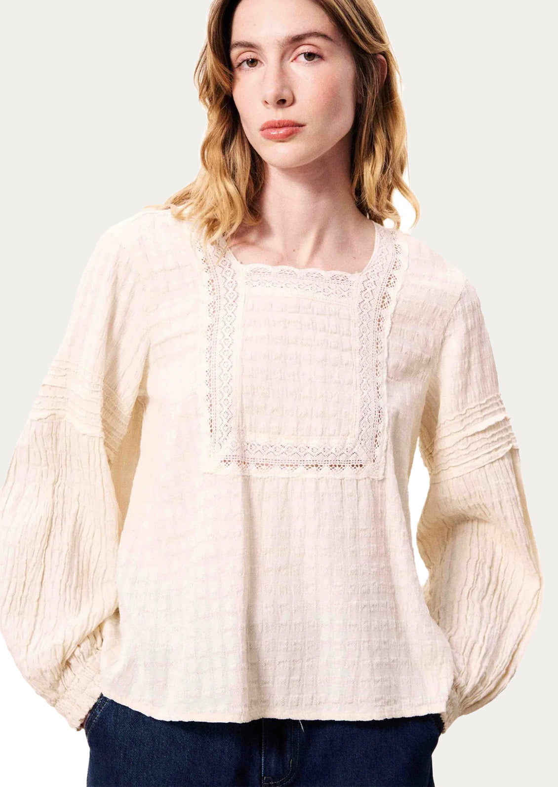 Woman wearing a cream blouse with lace details on a white background