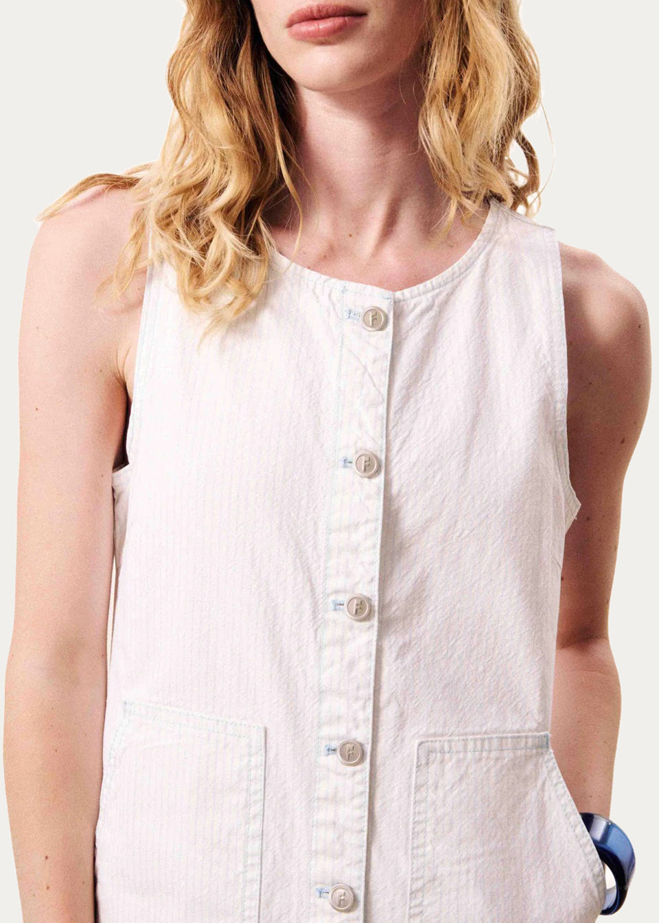 Woman wearing a white sleeveless button-up shirt against a plain background
