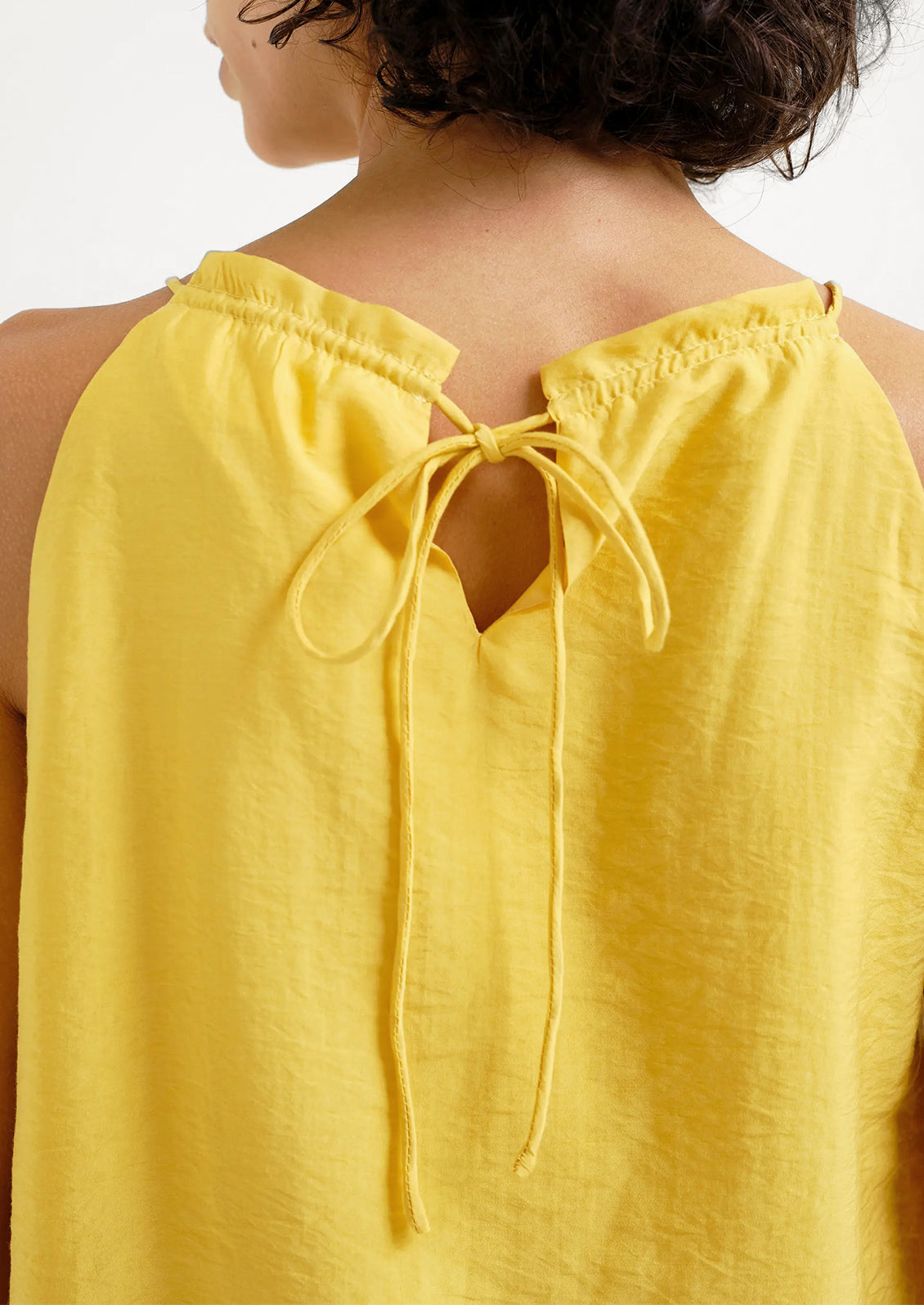 Yellow sleeveless top with open back and tie details on a white background