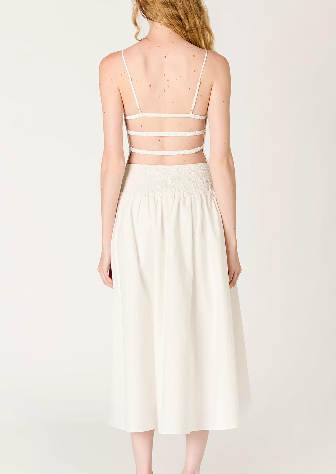 A person wearing a white dress with smocked bodice, full skirt and strappy open back.