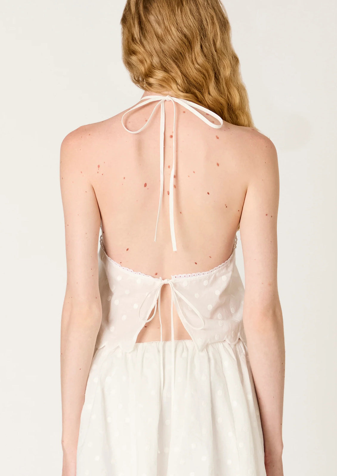 White polka dot halter top worn by a model on a plain background