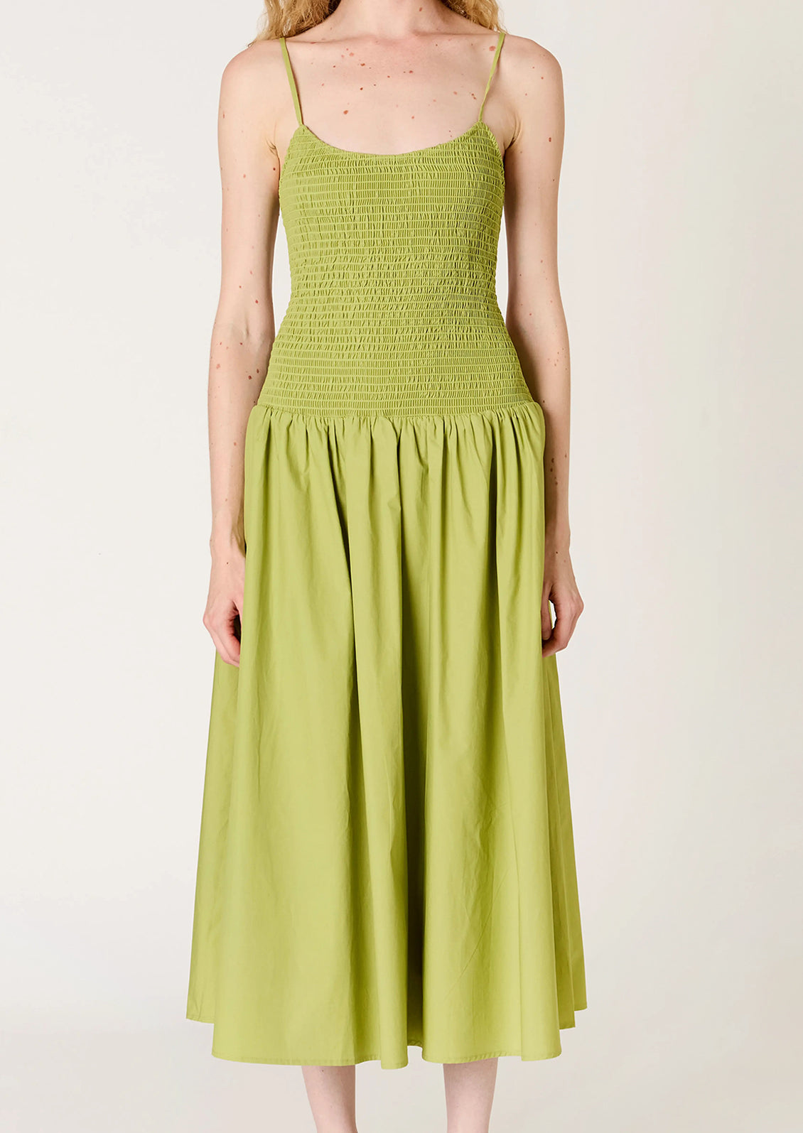 A person wearing a green dress with smocked bodice, full skirt and strappy open back.