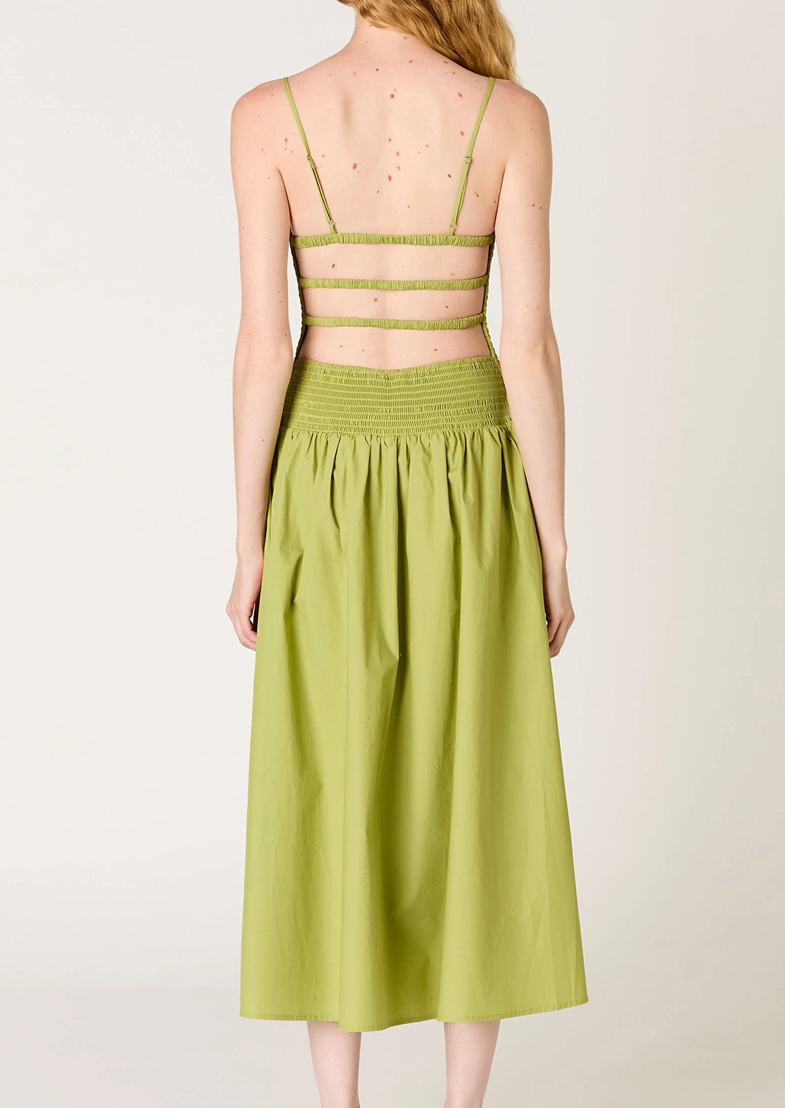 A person wearing a green dress with smocked bodice, full skirt and strappy open back.