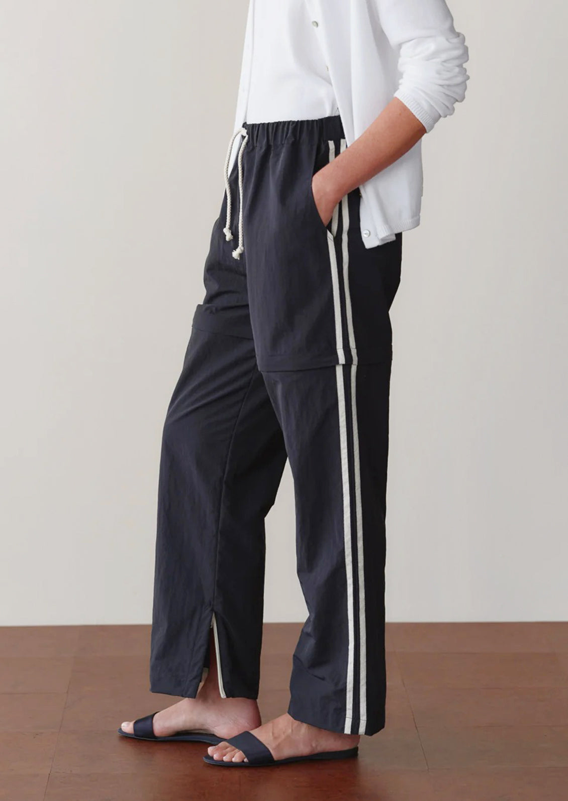 Person wearing black pants with white stripes and a white top against a neutral background