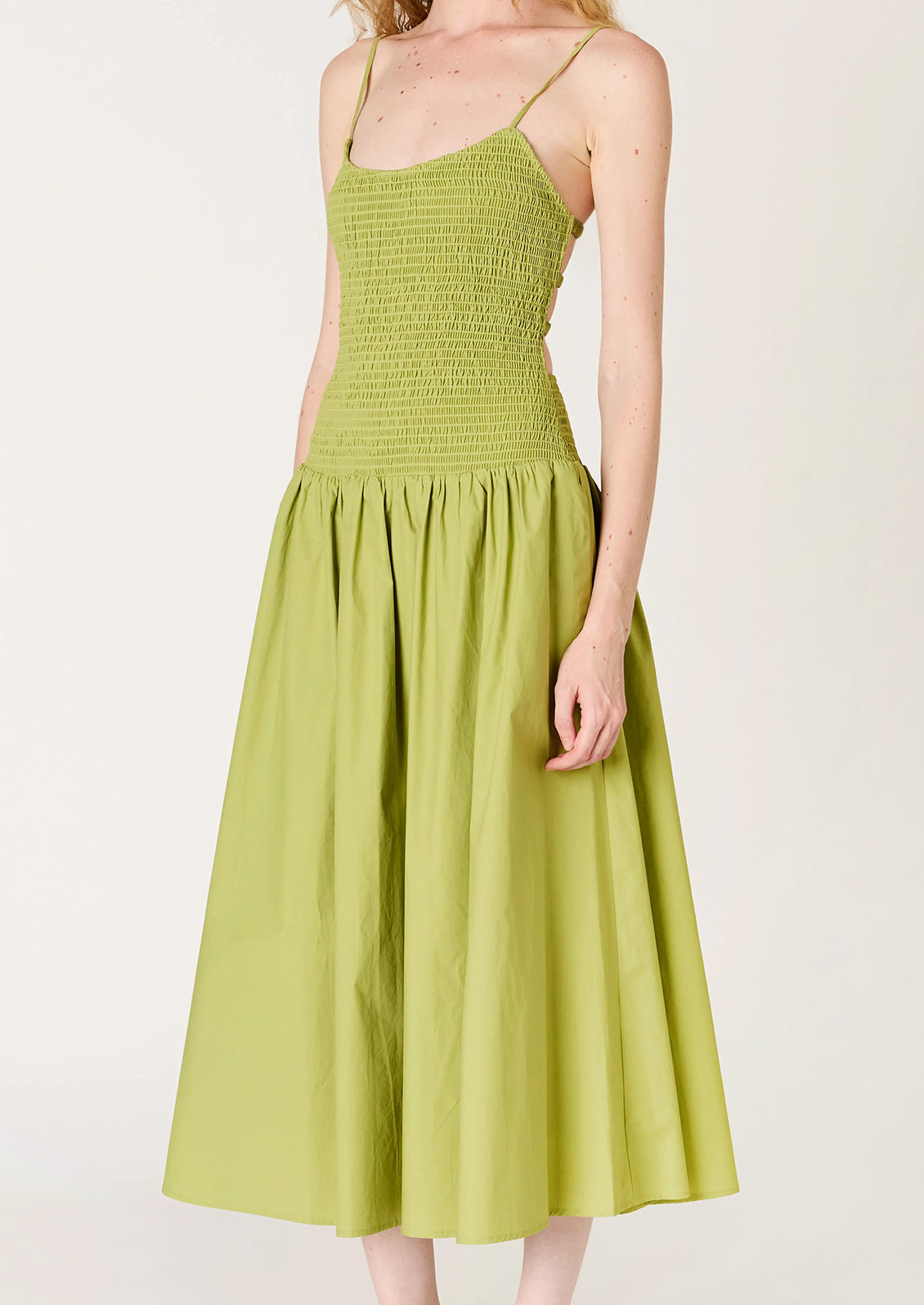 A person wearing a green dress with smocked bodice, full skirt and strappy open back.