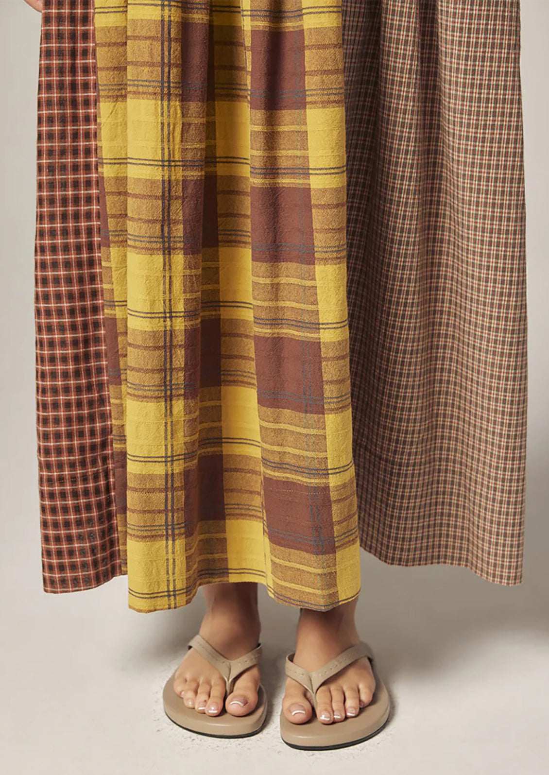 A person wearing a long plaid cotton dress in brown and yellow tones.