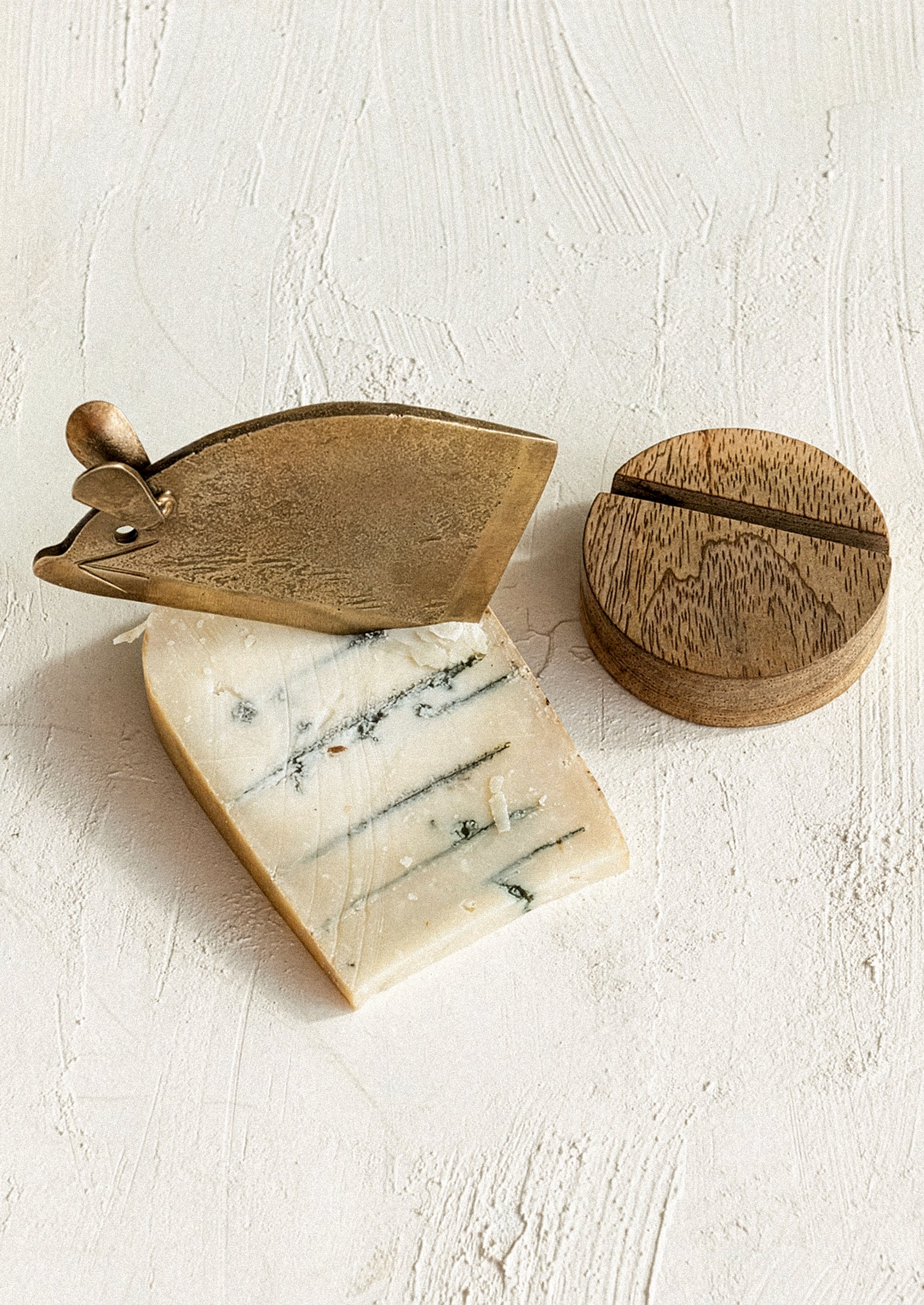 Cheese with a wooden cheese knife and round wooden cover on a light background