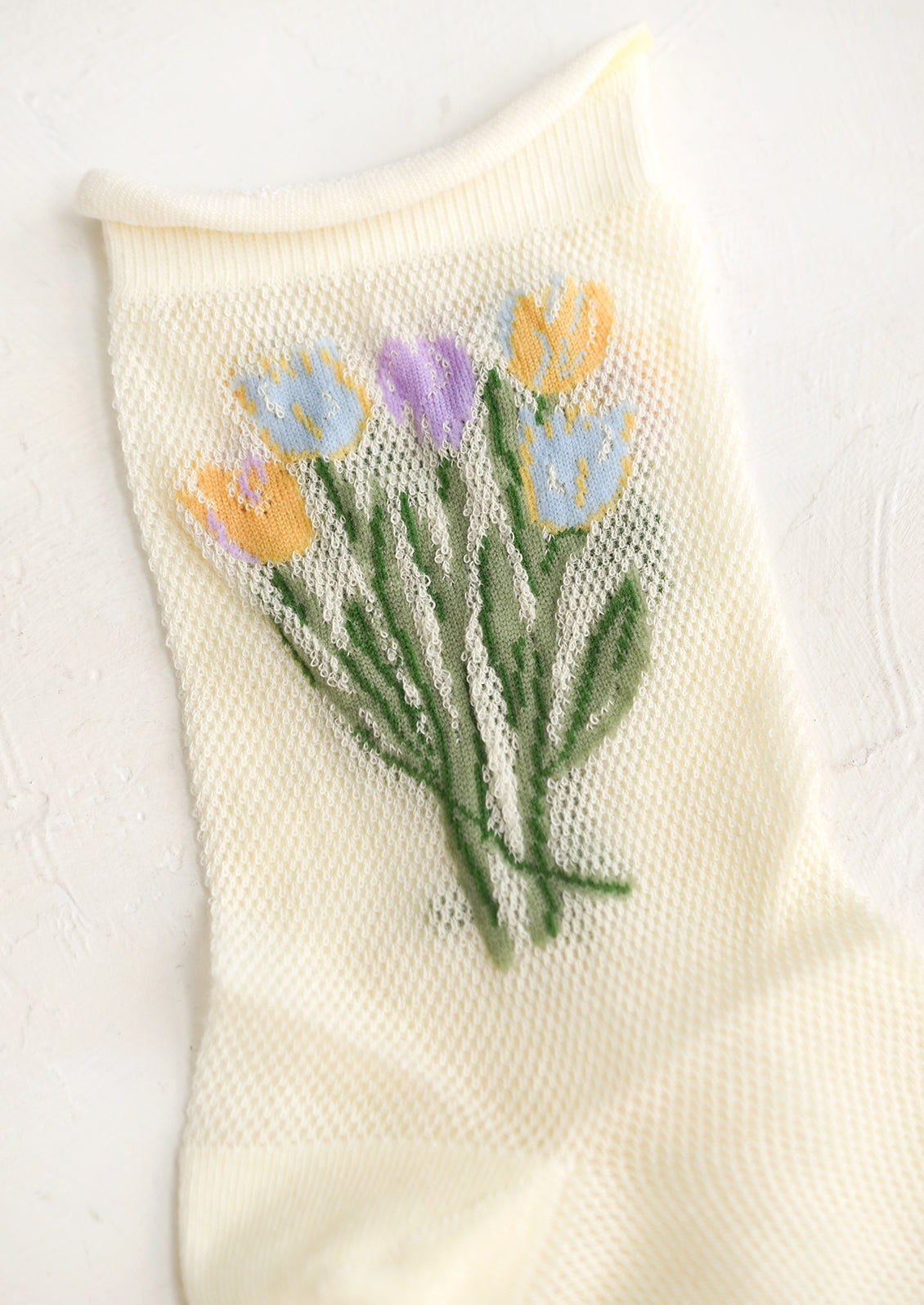 A pair of yellow mesh socks with multicolor tulip pattern at top.
