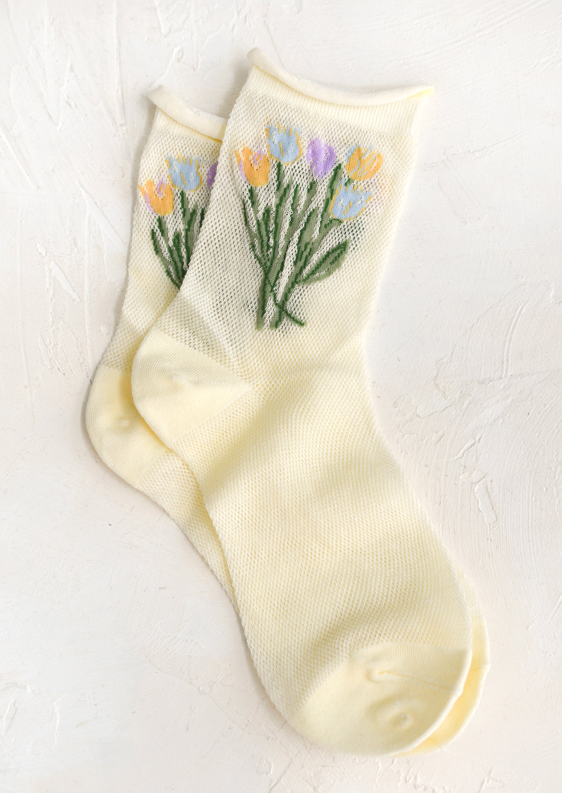 A pair of yellow mesh socks with multicolor tulip pattern at top.