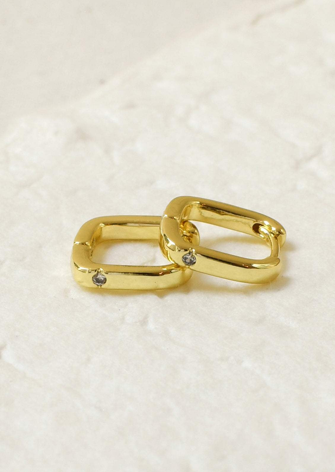 A pair of gold square shaped hoop earrings with a small crystal gem.