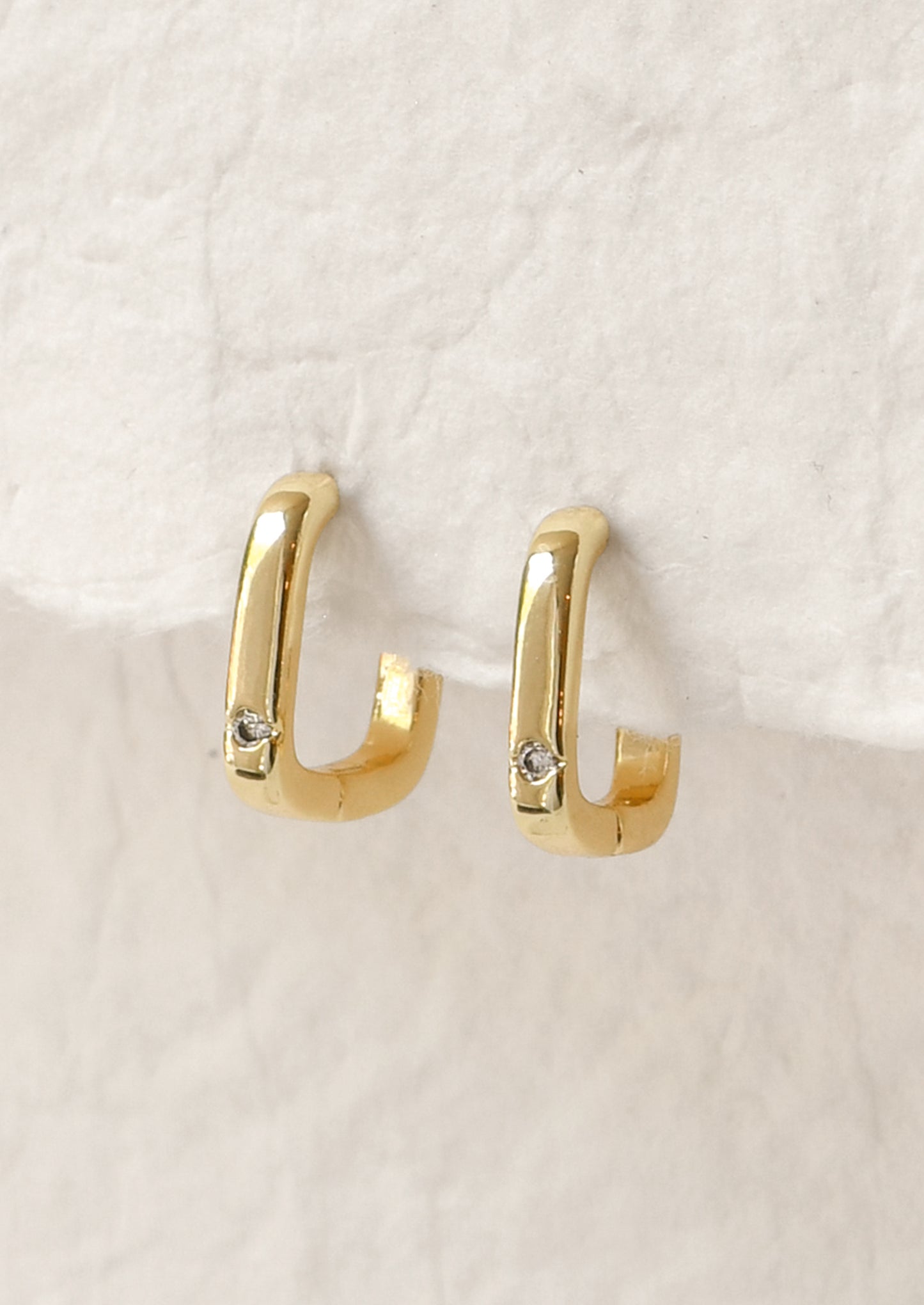A pair of gold square shaped hoop earrings with a small crystal gem.