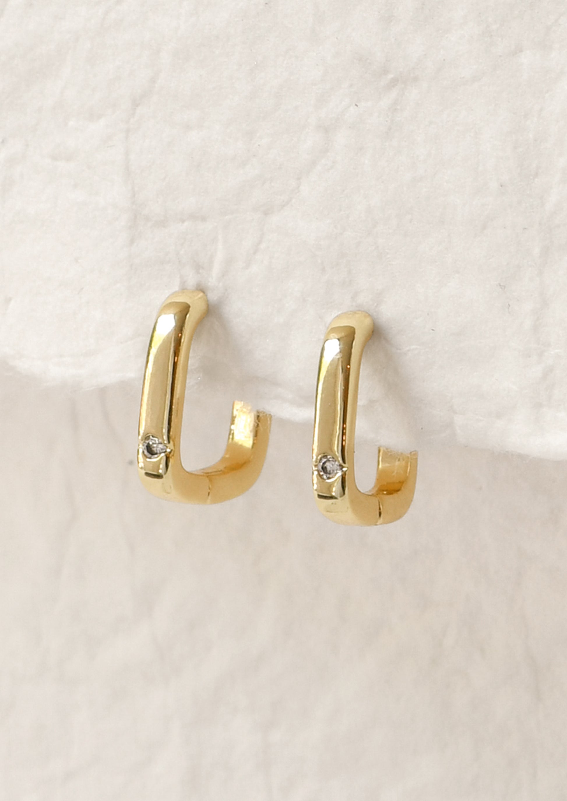 A pair of gold square shaped hoop earrings with a small crystal gem.