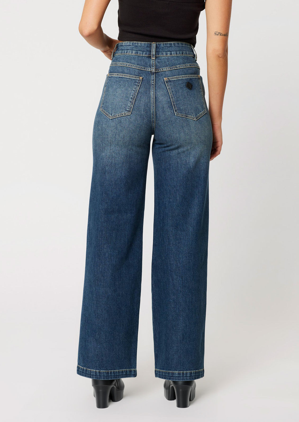A woman wearing a pair of wide leg, high rise jeans in medium dark blue wash with seam down center leg.