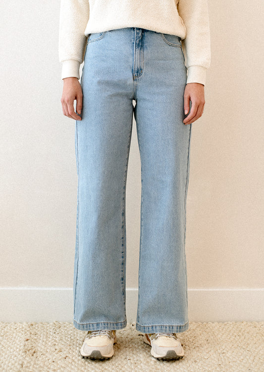 A woman wearing a pair of blue jeans with high rise and wide leg.