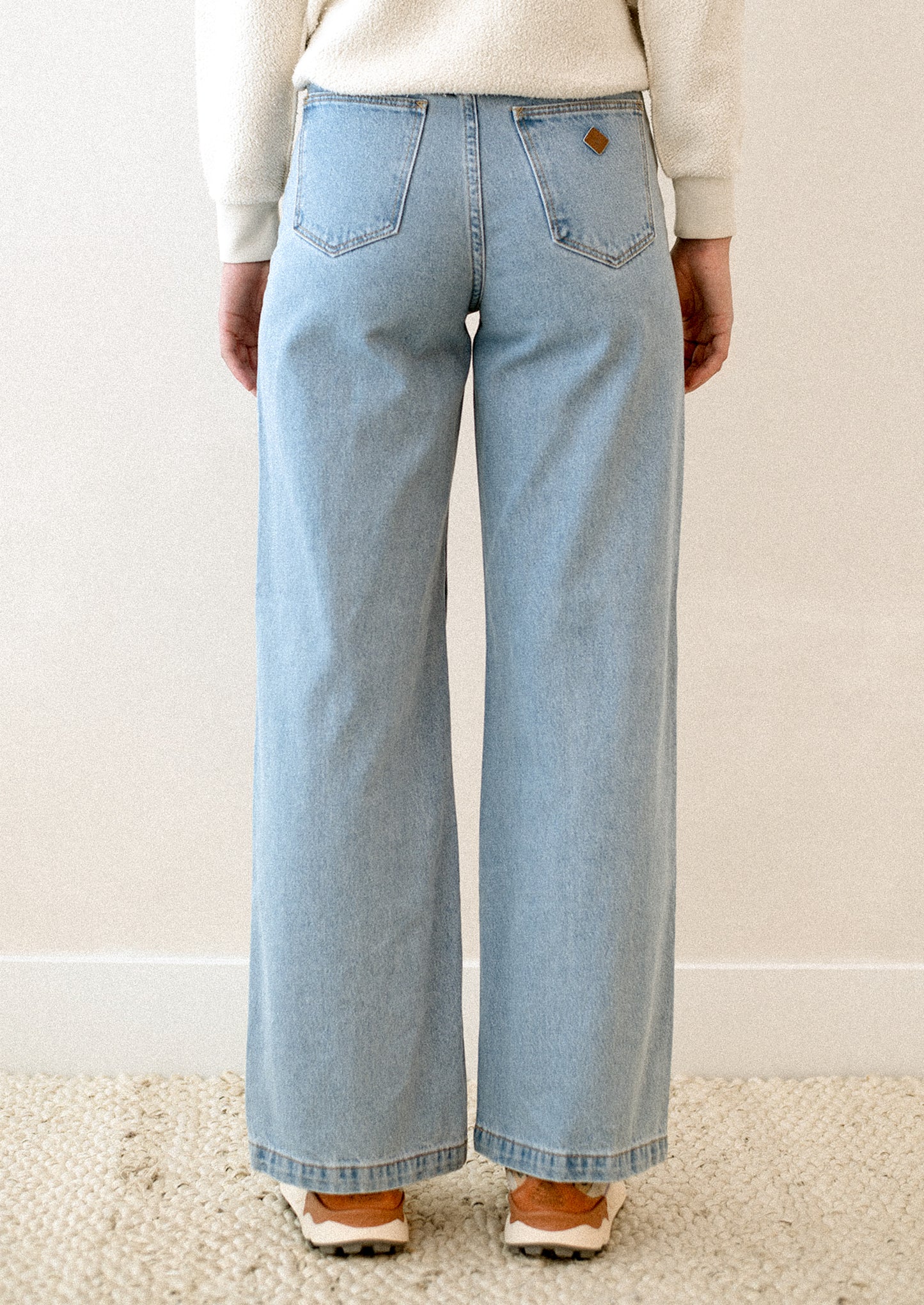 A woman wearing a pair of blue jeans with high rise and wide leg.