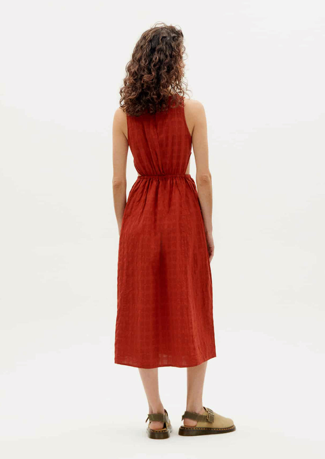 A woman wearing a rust-hued sleeveless dress with tonal square texture and cutout detail at waist.