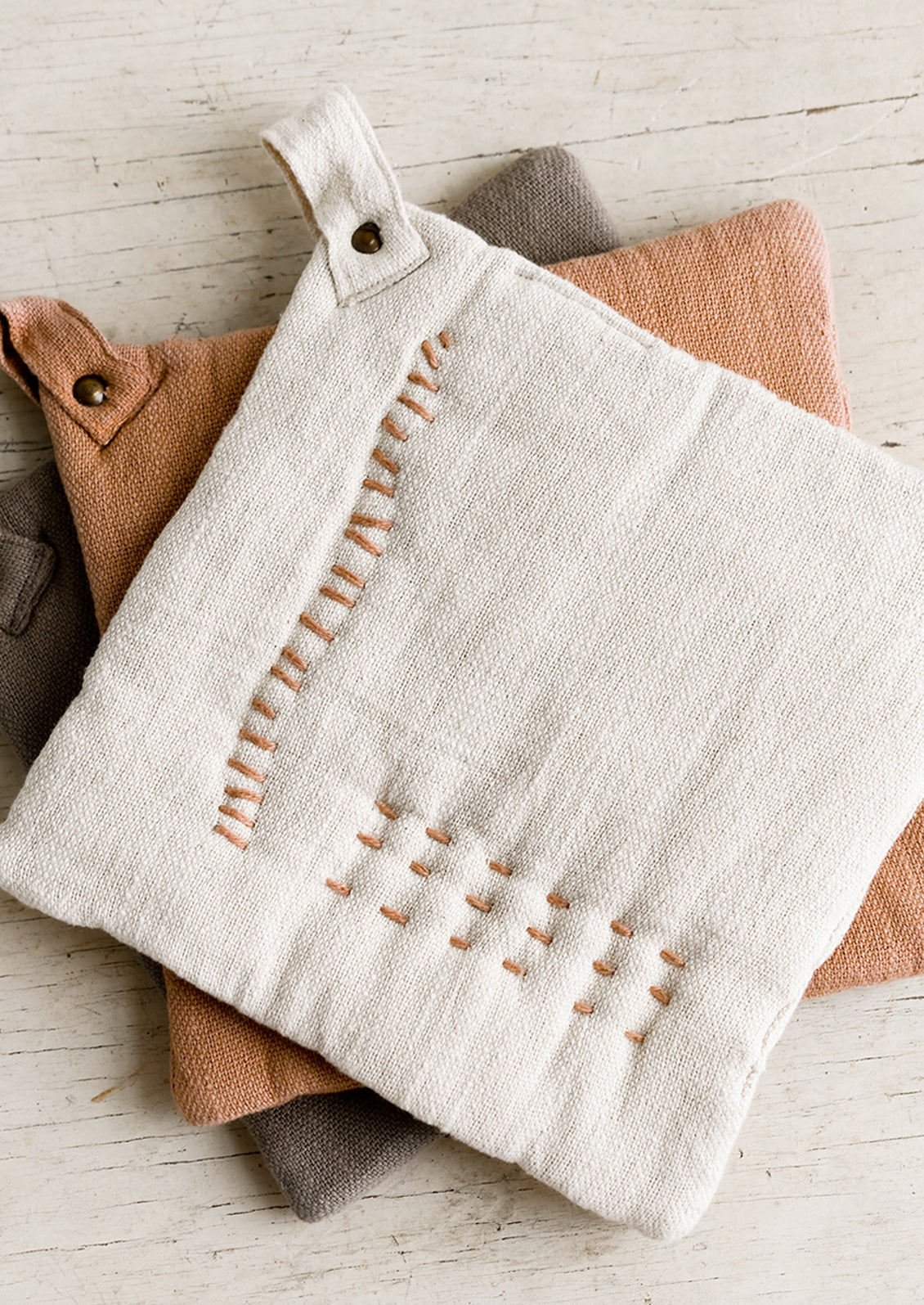 A stack of cotton potholders with decorative contrast stitching.