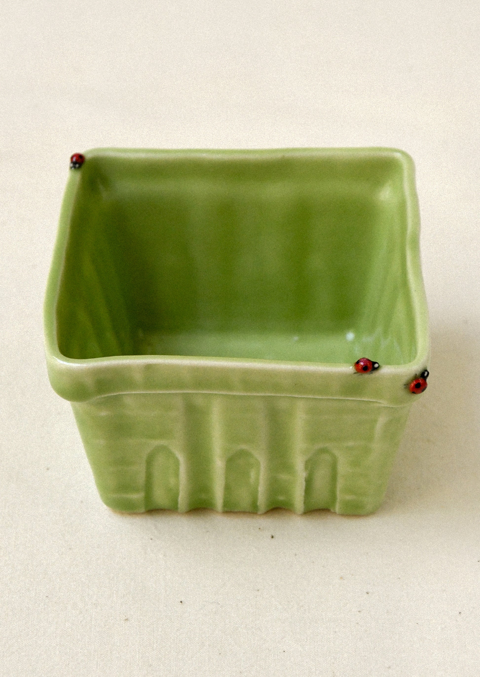 Green ceramic basket with red ladybugs on a beige background