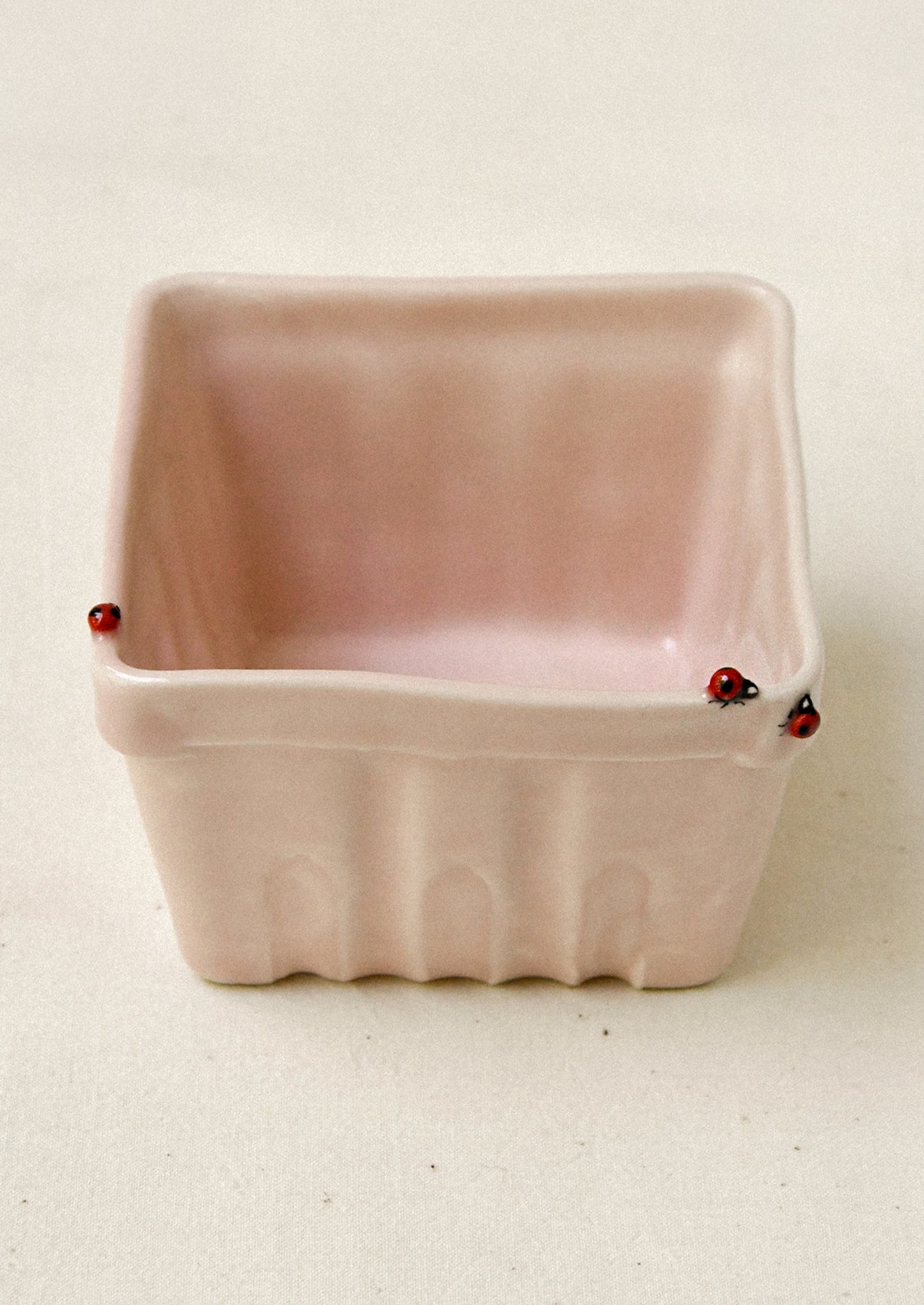 Pink ceramic basket with red ladybugs on a beige background