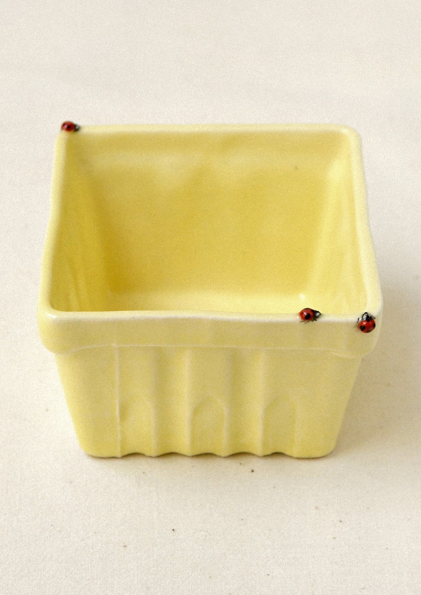 Yellow ceramic basket with red ladybugs on a beige background