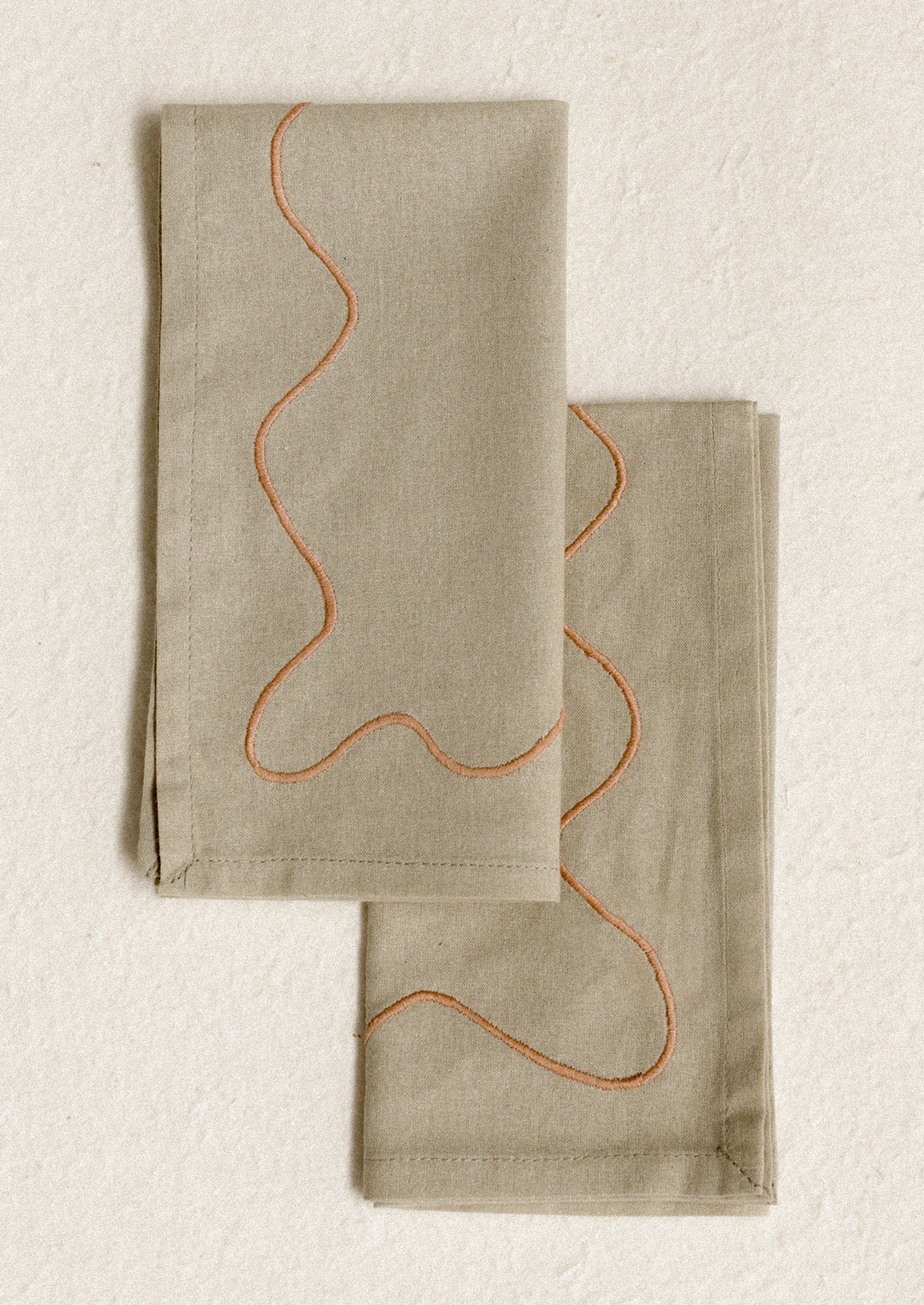 A pair of greige napkins with peach squiggle embroidery.
