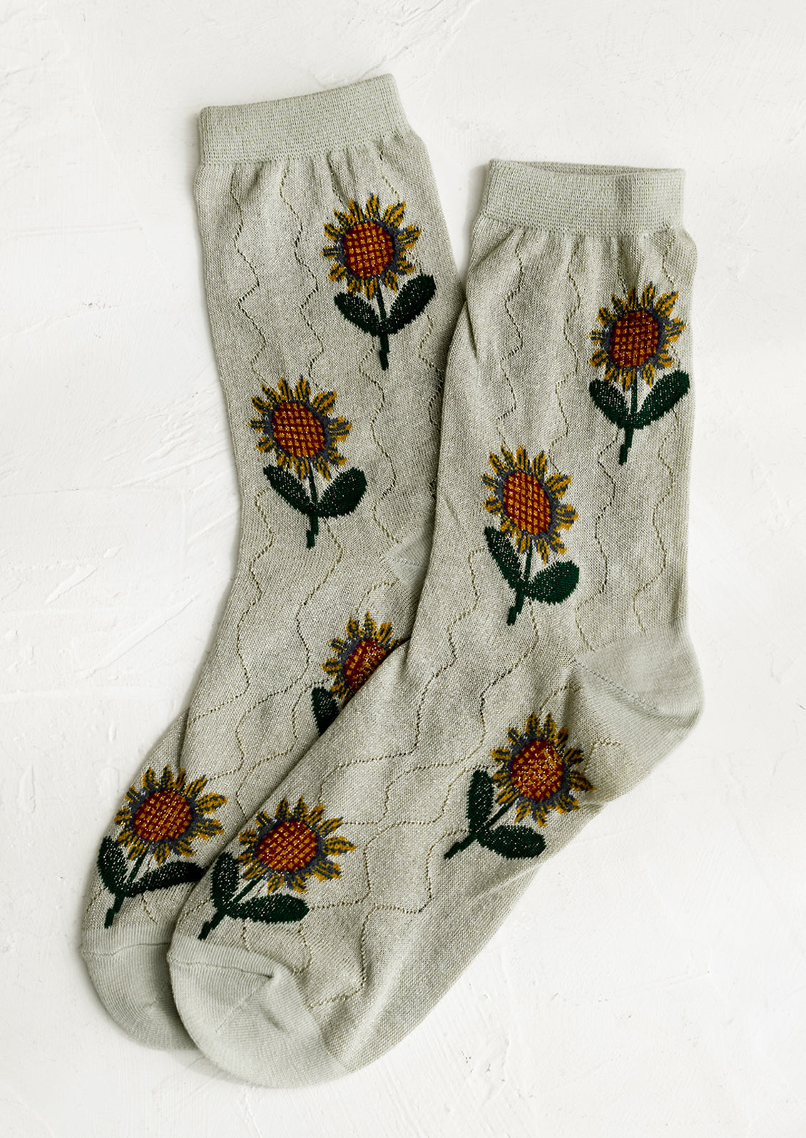 A pair of seafoam colored socks with sunflower pattern.