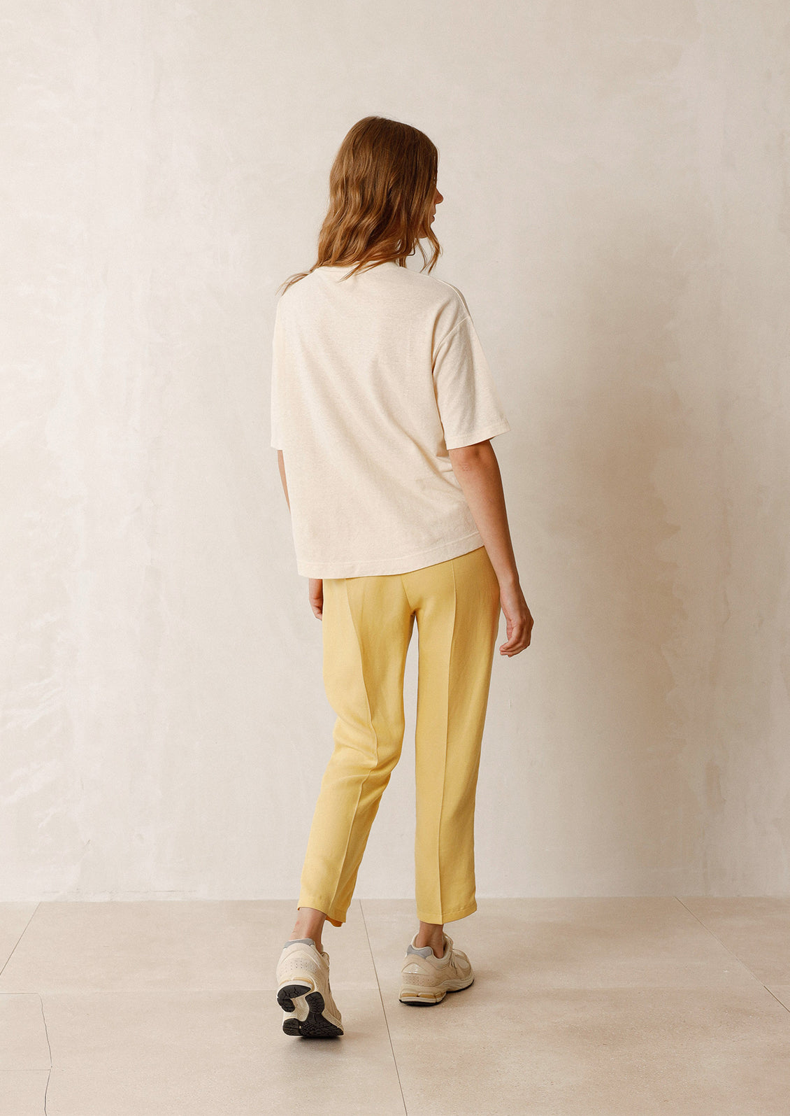 Woman wearing ecru tee, yellow pants, and sneakers, seen from behind. 