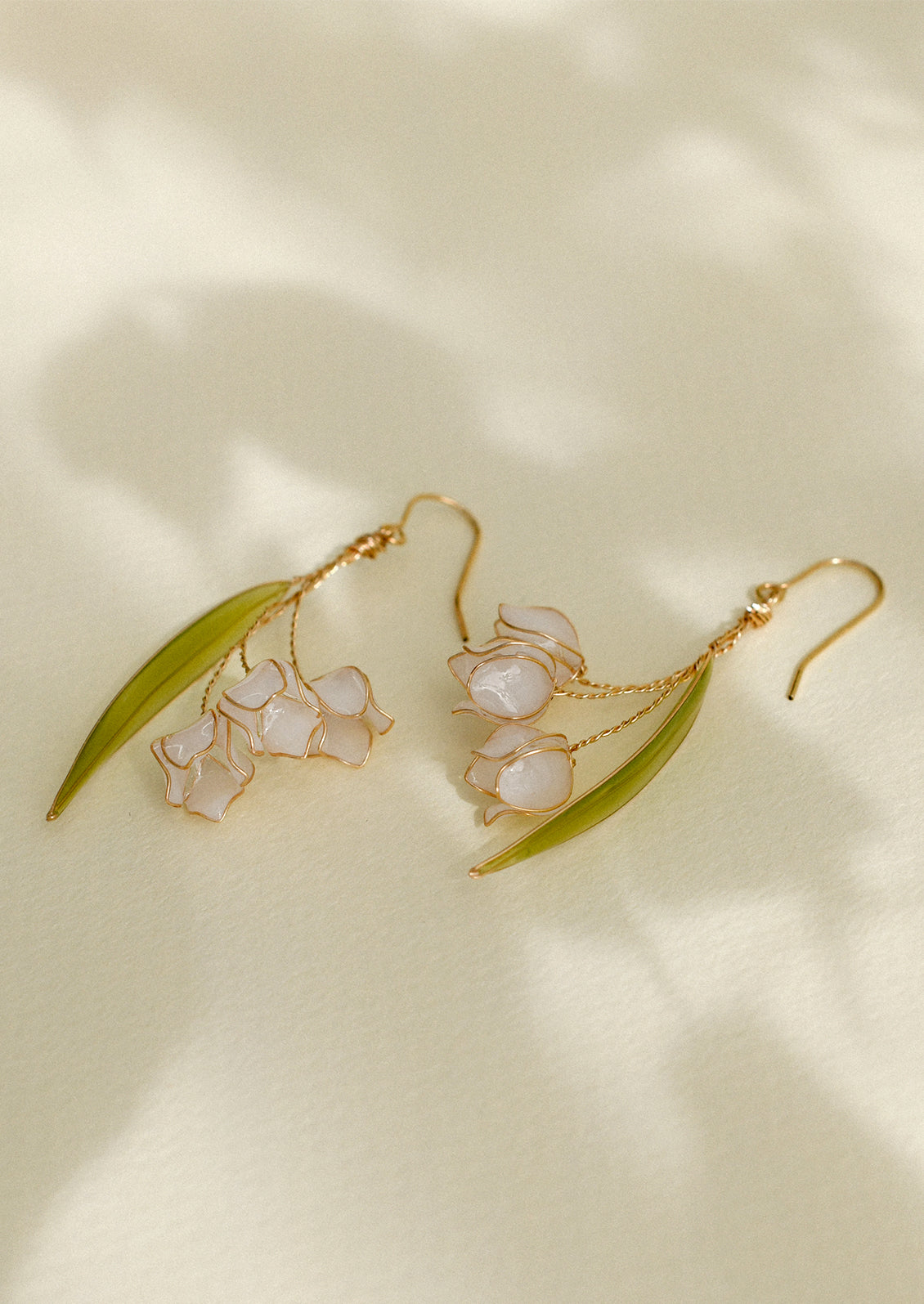 A pair of delicate resin and gold earrings resembling lily of the valley flower.