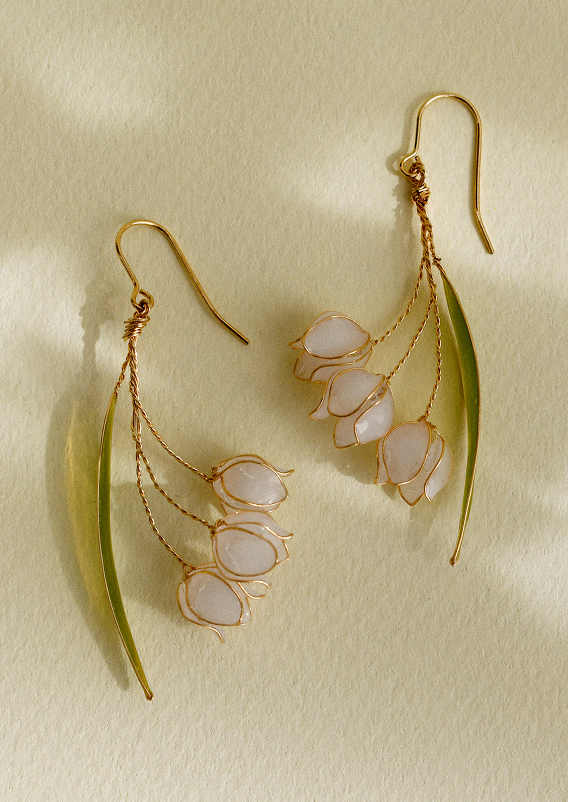 A pair of delicate resin and gold earrings resembling lily of the valley flower.