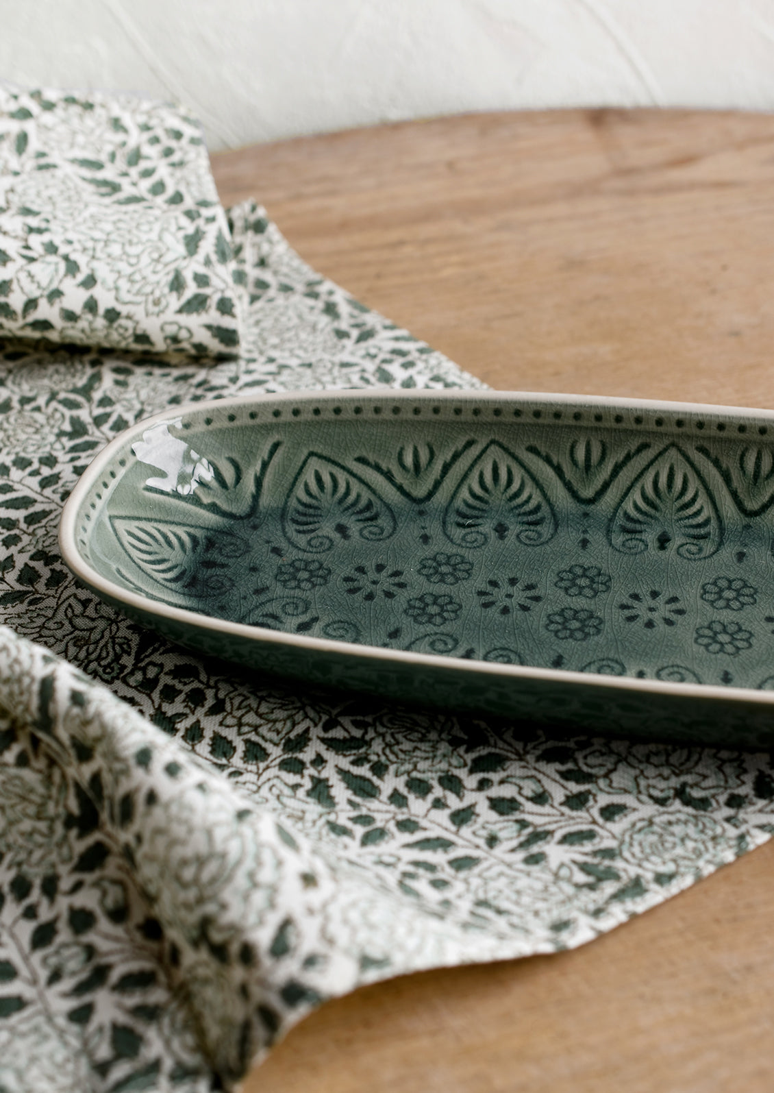 An oblong, curved platter in glossy green glaze with Polish inspired pattern.