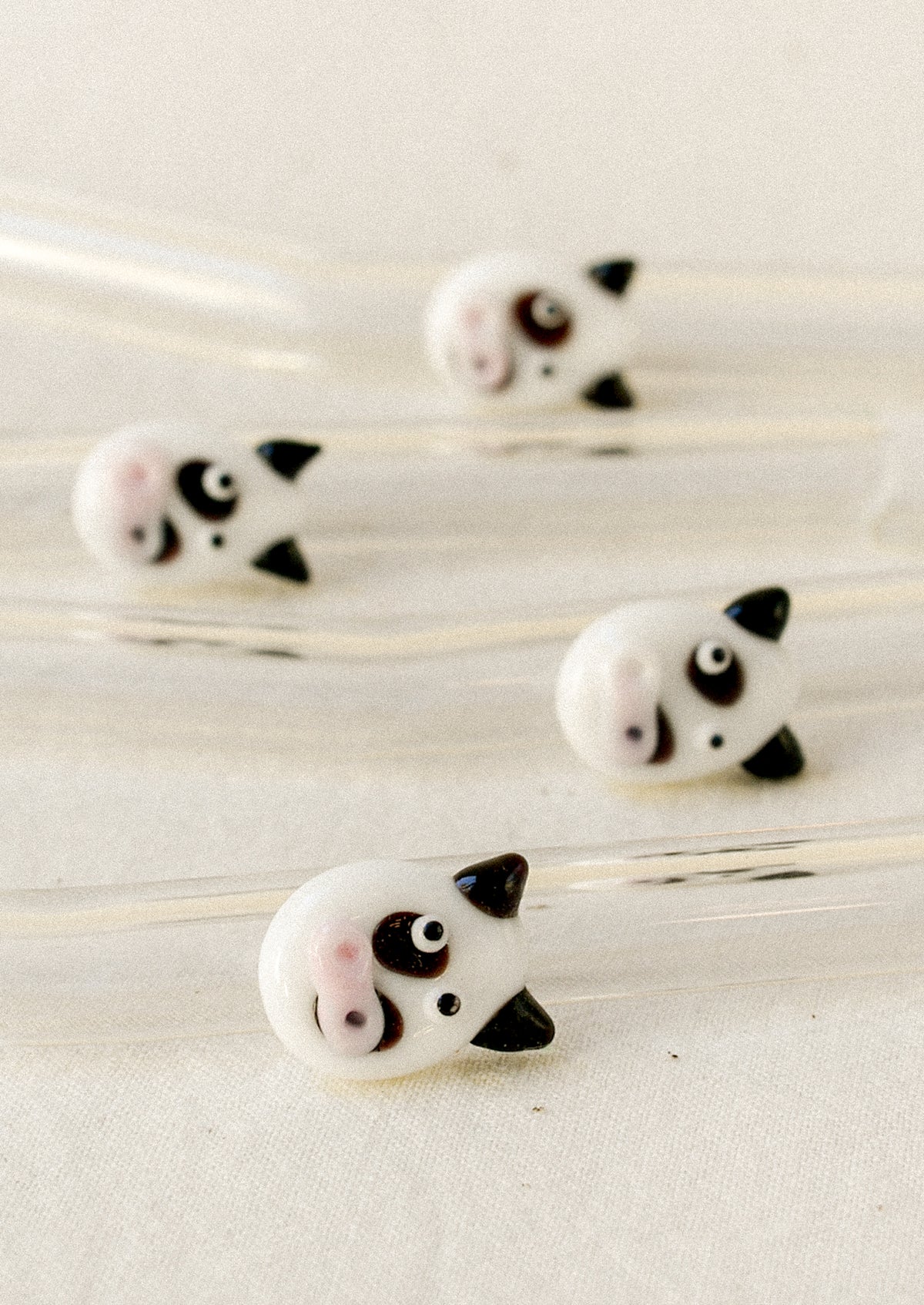 Four glass straws with cow faces on them.