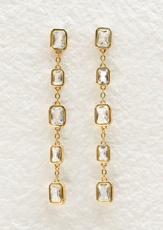 A pair of long gold dangling earrings with large rectangular gems.