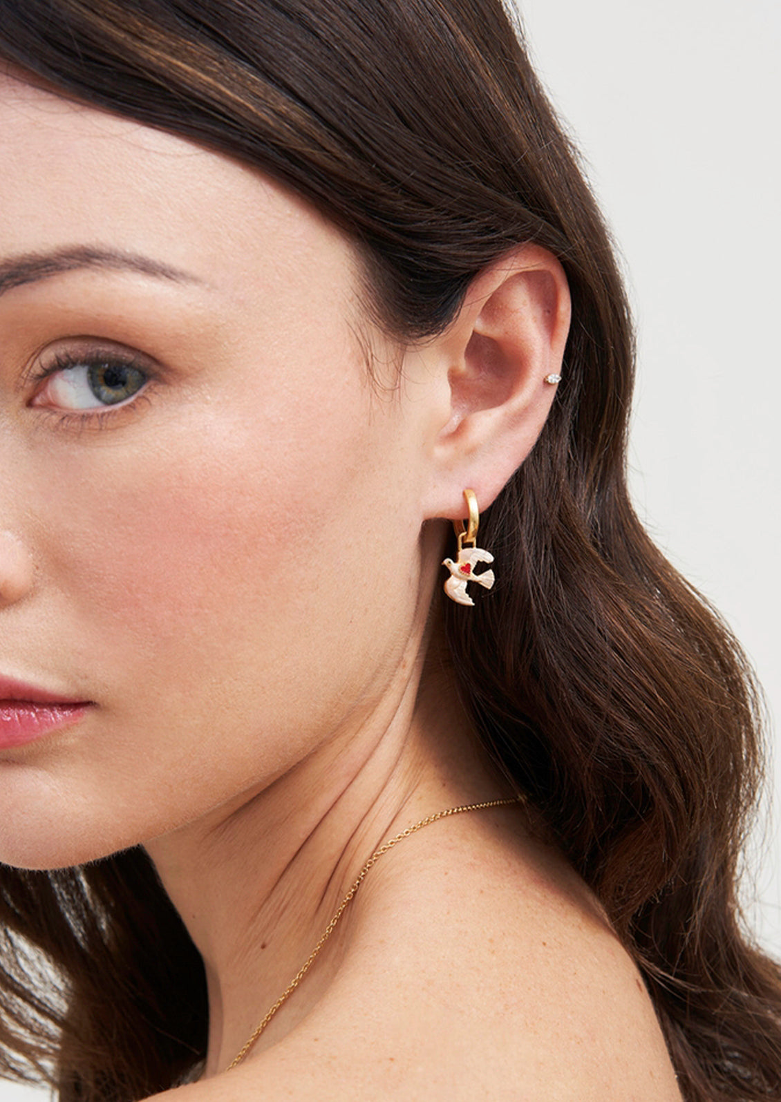 A pair of gold hoop earrings with dove charms adorned with a red heart.