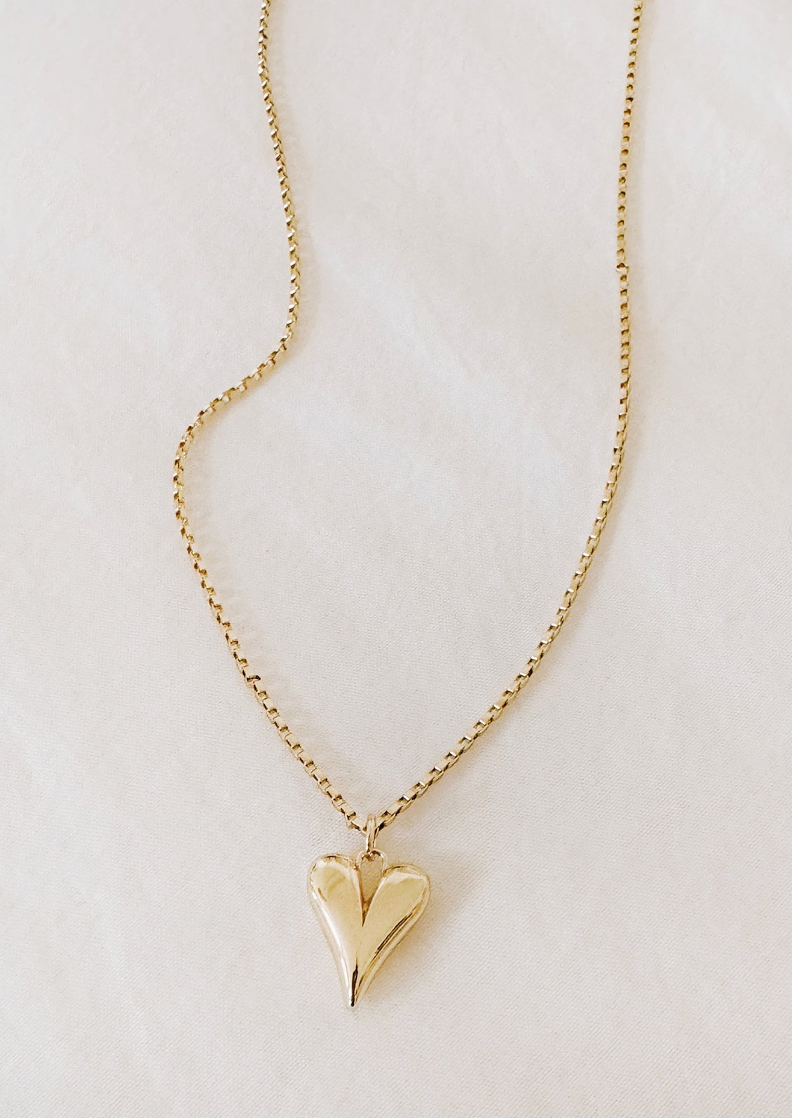 A gold necklace with box chain and small heart pendant.
