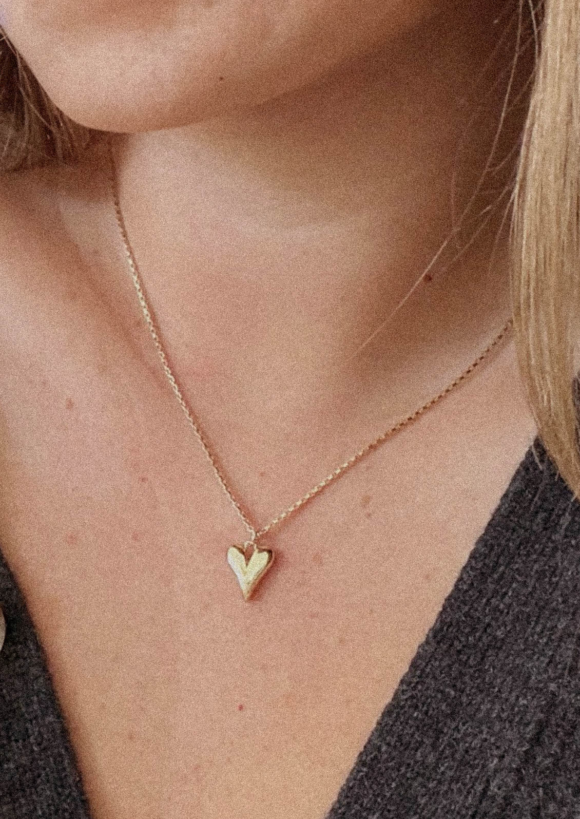 A gold necklace with box chain and small heart pendant.