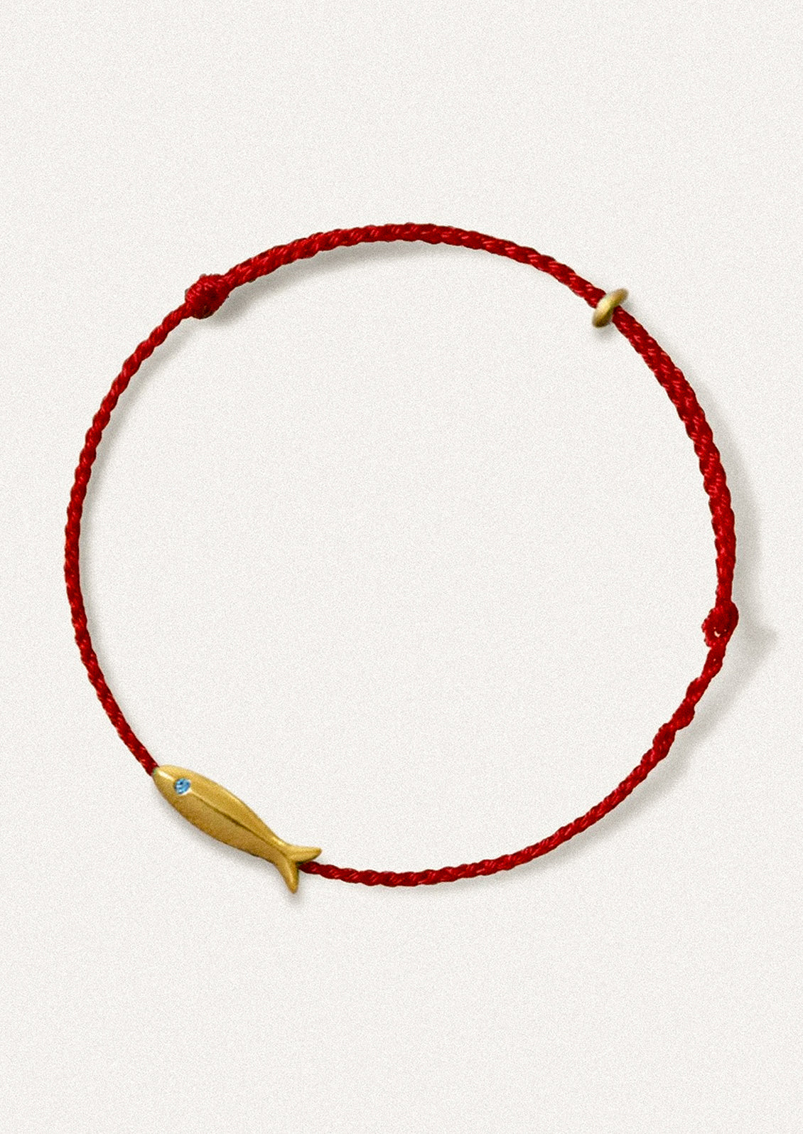 A red cord bracelet with gold fish charm.