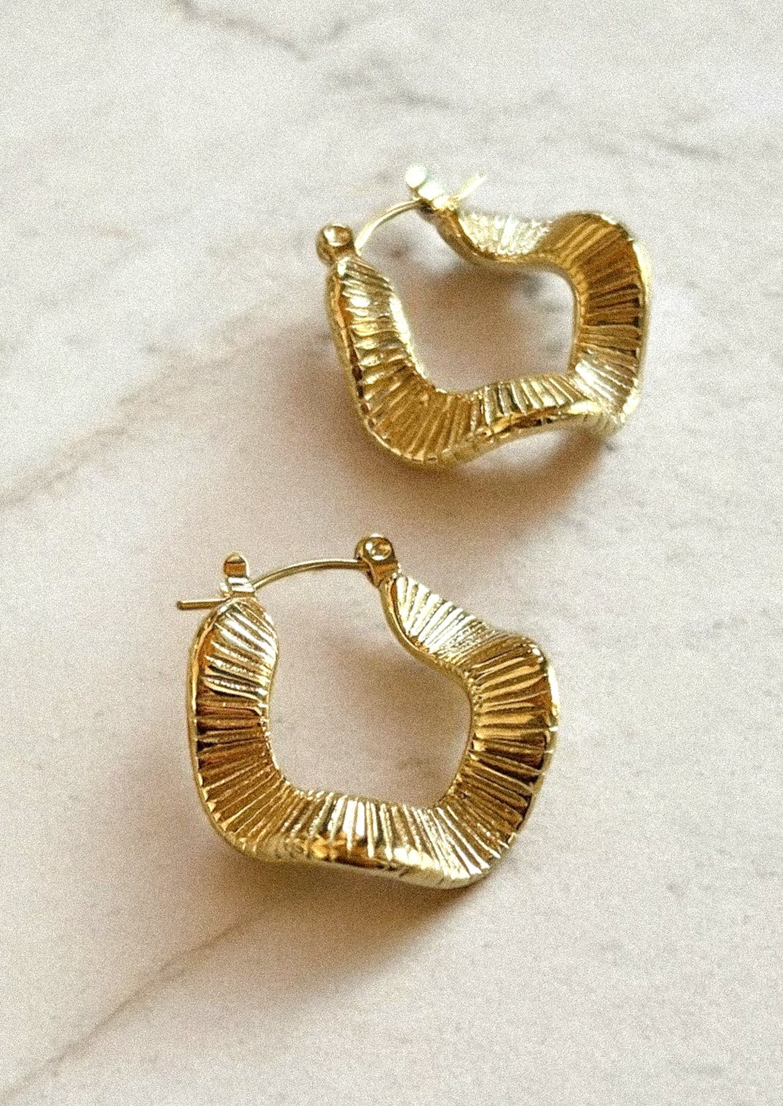 A unique pair of gold plated hoop earrings with a wavy shape.