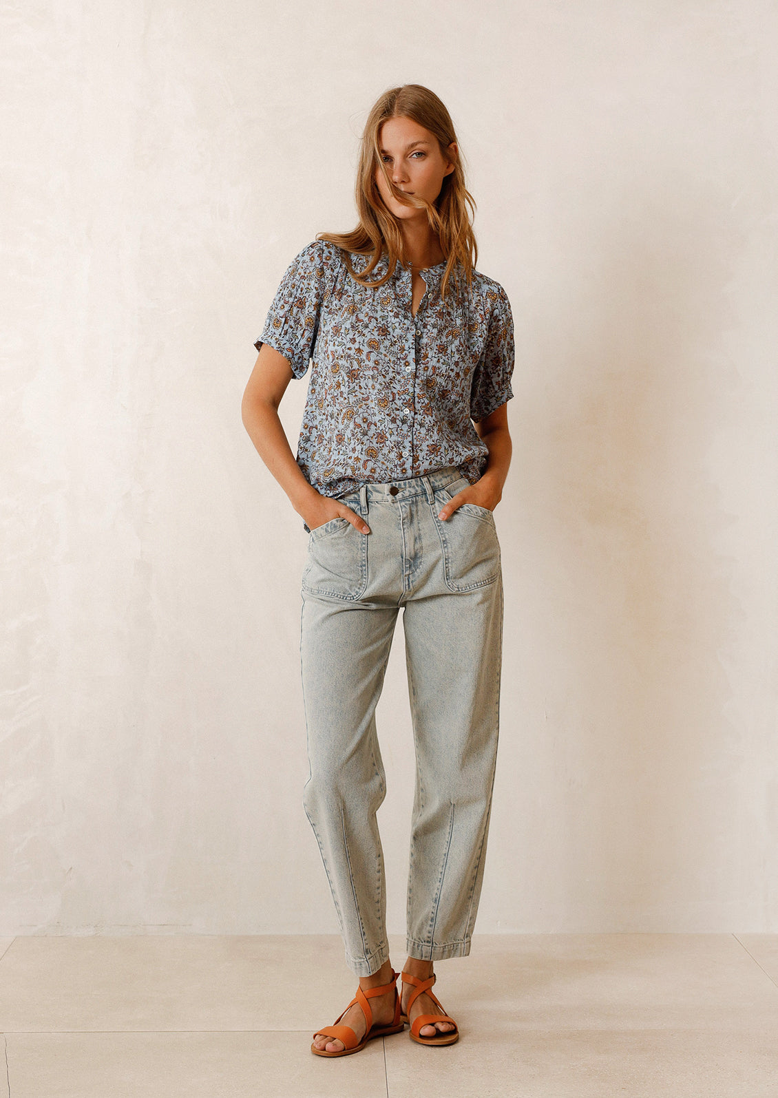 Woman wearing blue and brown printed top, blue jeans, and sandals. 