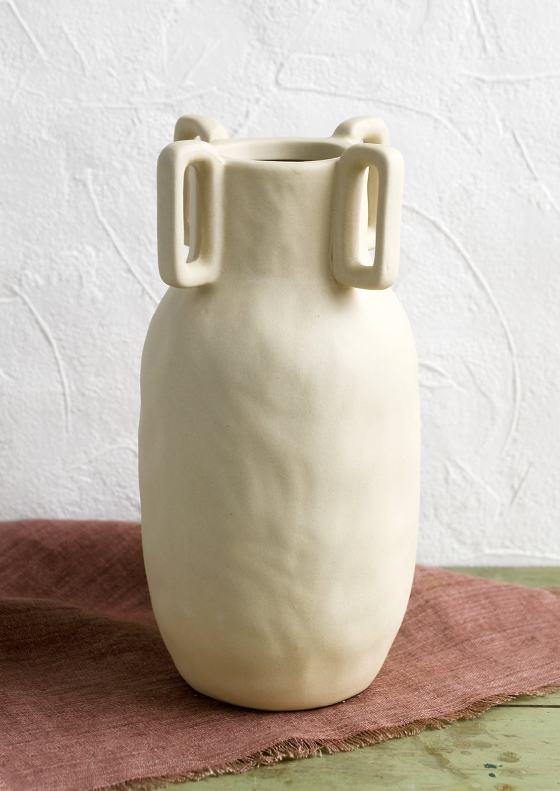 A sand color vase in matte ceramic with decorative square handle detail around mouth.