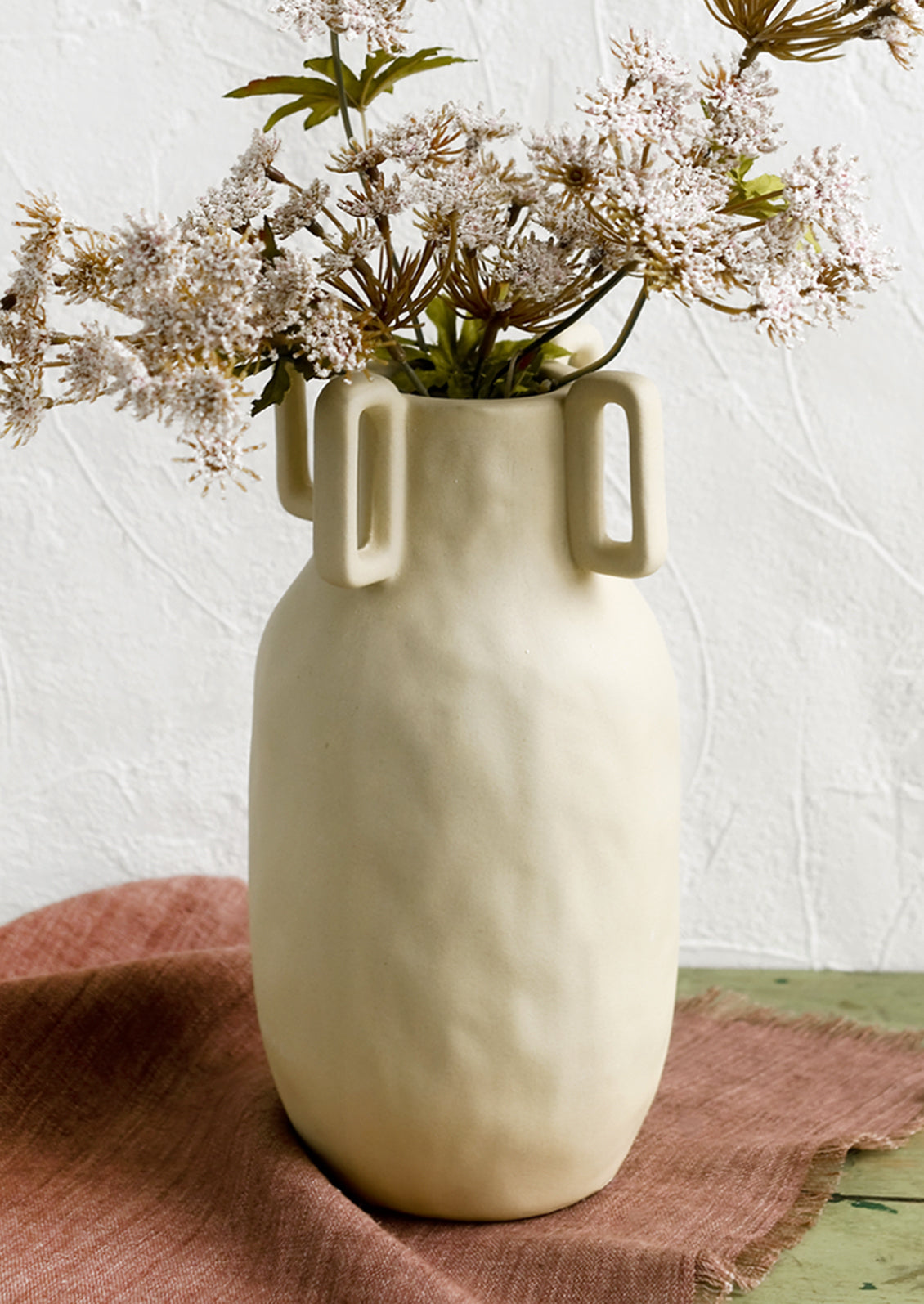 A sand color vase in matte ceramic with decorative square handle detail around mouth.