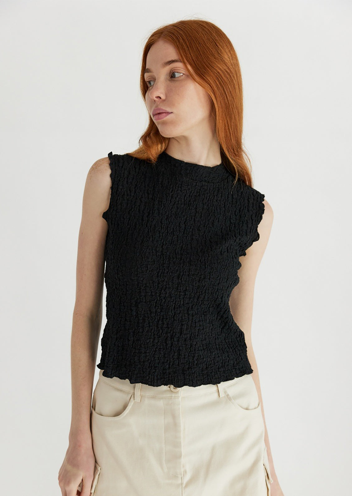 A woman wearing a sleeveless black top with crinkled texture.