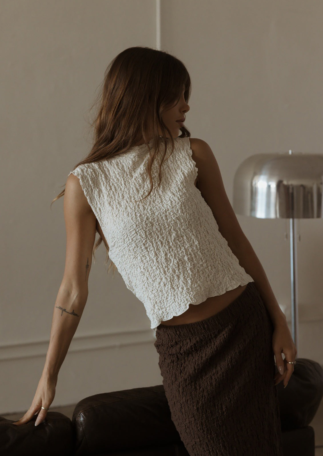 A woman wearing a sleeveless cream top with crinkled texture.